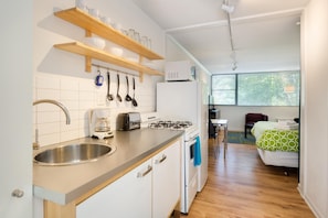 A compact kitchen with a sink, stove, and toaster, and a bedroom with a bed and window. - CCF Enjoy a Full Kitchen in an Affordable Studio Near Peachtree Street (Atlanta)