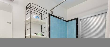 A modern bathroom with a shower, a black metal shelf unit, and a blue-tiled wall.