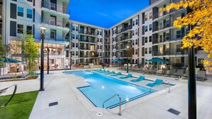 Ein moderner Apartmentkomplex mit einem zentralen Schwimmbad, mehreren Balkonen und Sitzbereichen im Freien.