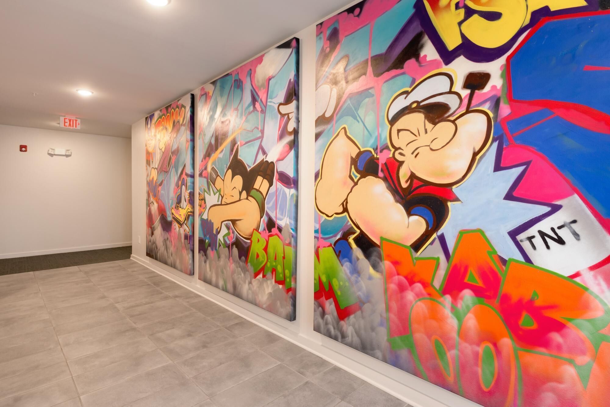 A hallway with colorful graffiti art on the walls and an exit sign.