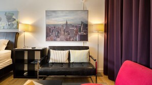 A modern hotel room with a black leather sofa, a red armchair, a black side table, a white bed, and a cityscape painting on the wall. - CCK Modern Studio Walkable to Midtown 1 Block From Marta (Atlanta)