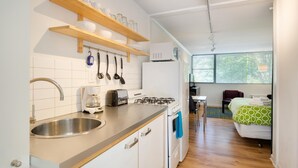 A modern kitchen with a stainless steel sink, a coffee maker, a toaster, and a stove. There are wooden shelves above the counter holding dishes and glasses. A window provides natural light to the room. - CCK Modern Studio Walkable to Midtown 1 Block From Marta (Atlanta)