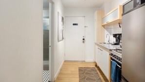 Une petite cuisine équipée d’un réfrigérateur, d’une cuisinière et d’une machine à café. On peut voir une porte sur laquelle est apposé un panneau indiquant qu’il est interdit de fumer.