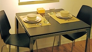 Une table à manger dressée avec des assiettes, des verres et des couverts, entourée de chaises, et un tableau encadré accroché au-dessus.