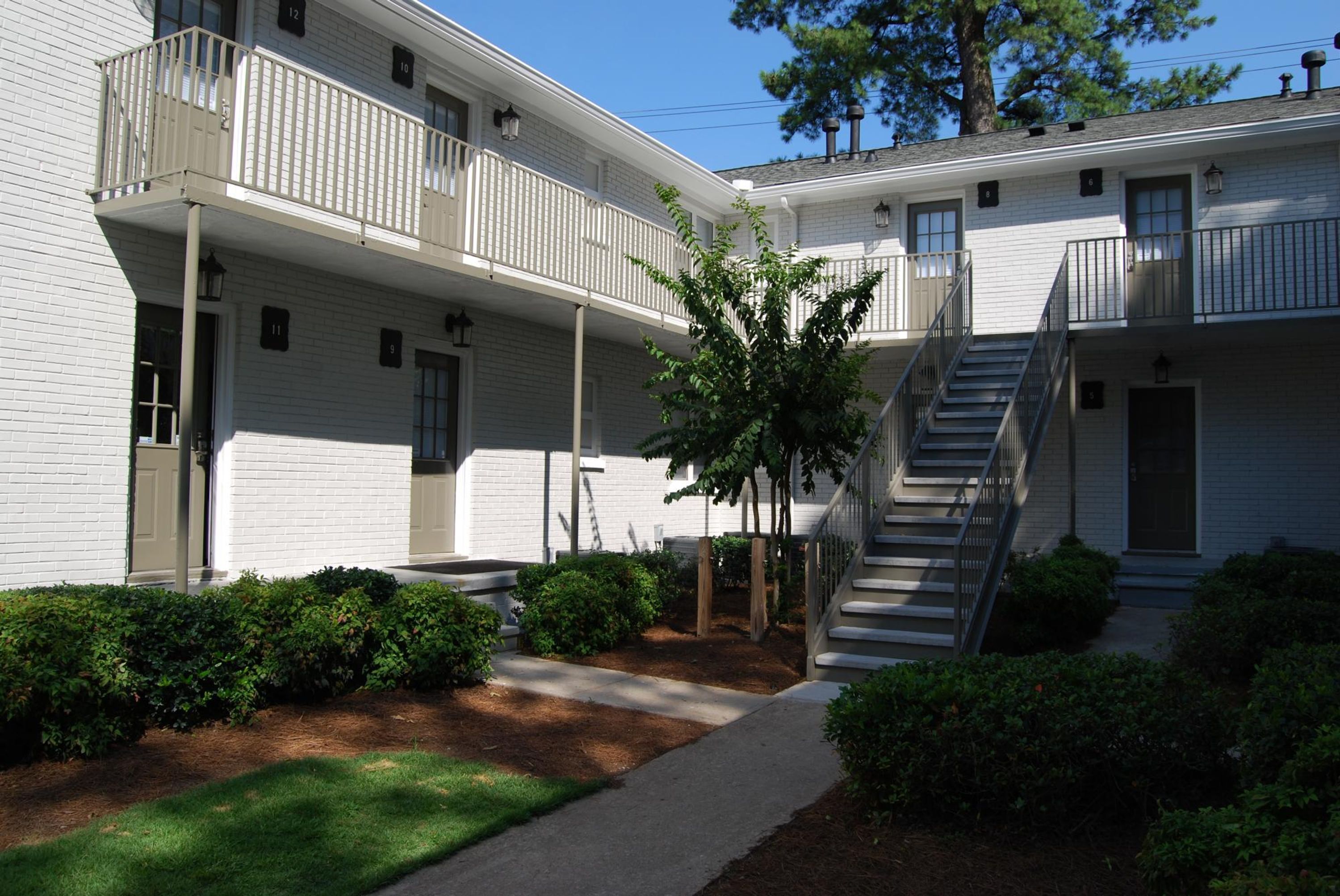 A two-story building with a central courtyard, a staircase, and a small tree.