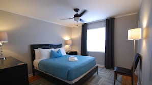Een hotelkamer met een bed, bureau, stoel, plafondventilator en raam met gordijnen.