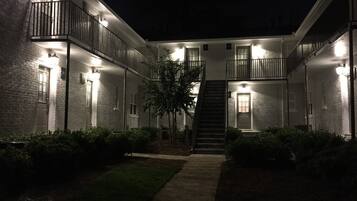 Un edificio de varios pisos con una escalera central, rodeado de balcones bien iluminados y un camino que lleva a la entrada.