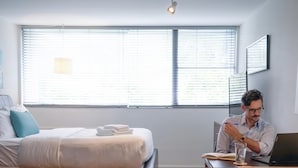 A bedroom with a bed, a desk with a laptop, and a window with blinds. - CPH Secluded Studio Safe Serene and Serviced (Atlanta)