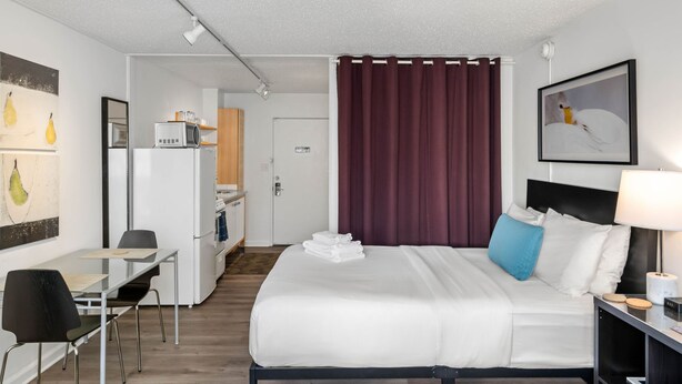 A hotel room with a bed, a desk with a chair, a microwave, a refrigerator, and a door leading to a kitchenette. - CCC Clean Cozy Convenient Studio in Buckhead w Free Parking (Atlanta)