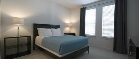 A bedroom with a bed, two bedside tables, a ceiling fan, and windows with curtains.