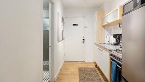 A narrow kitchen with a refrigerator, stove, and coffee maker. A door with a 'No Smoking' sign is visible. - CPE Safe Quiet Studio w Comfortable Bed (Atlanta)
