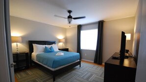 A neatly arranged hotel room with a bed, bedside lamps, a desk with a computer, and a ceiling fan.