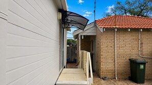 A narrow outdoor corridor with a metal staircase leading to a covered area, a brick wall, and a green trash bin with the number 58.