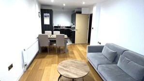 A modern living room with a grey sofa, a round coffee table, and a dining area with a table and chairs. - Charming 1-bed Apartment in London (London)