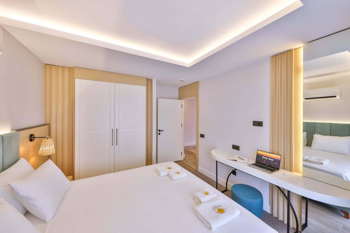 A hotel room with a bed, a desk with a laptop, a mirror, and a wardrobe.