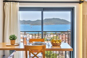 A dining area with a table set for two, a potted plant, and a view of the sea and mountains. - Sole Vista Homes  (Kas)