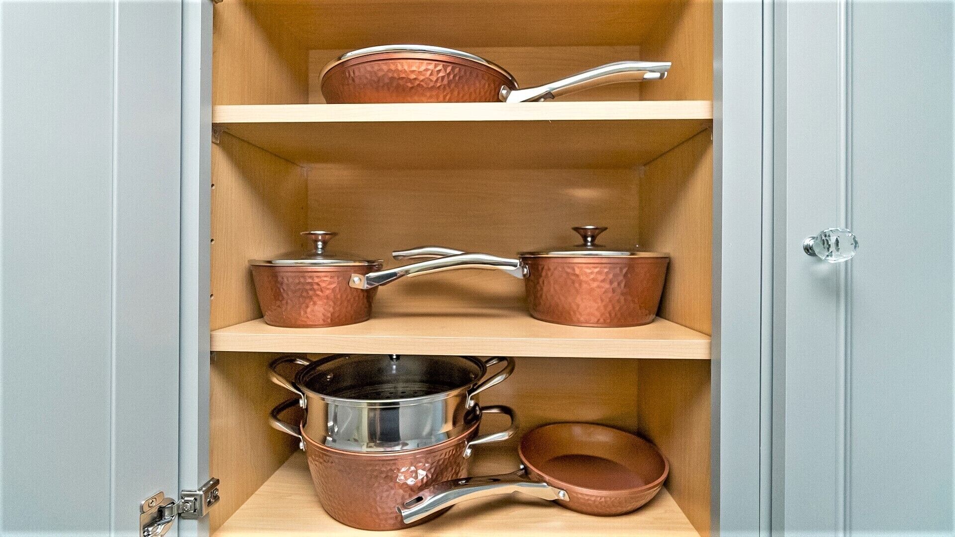 Ein Küchenschrank mit drei Einlegeböden, auf denen Kupferkochgeschirr steht.