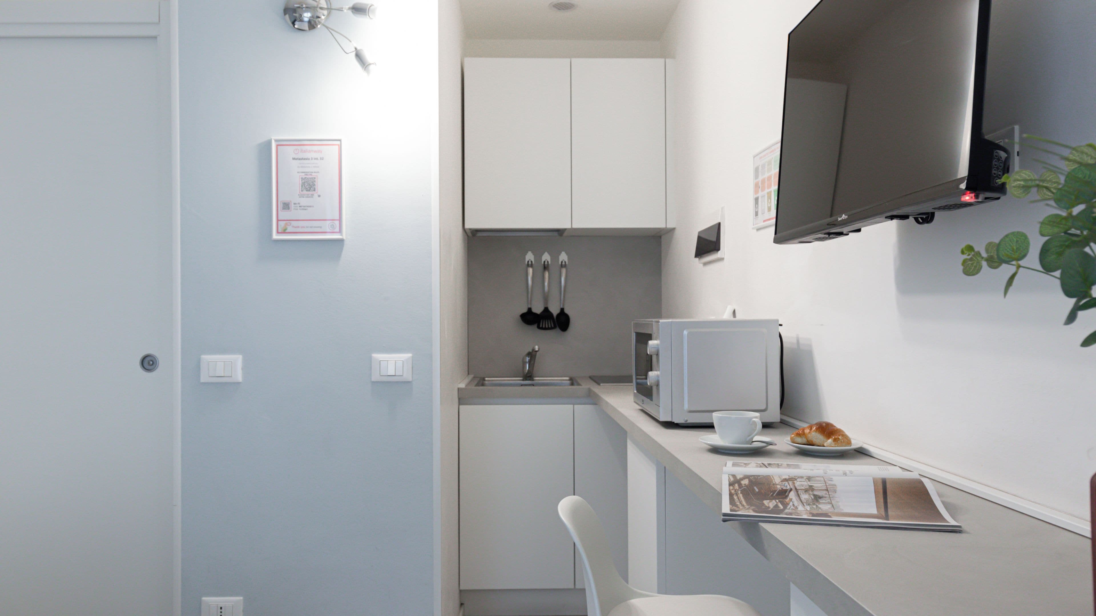 A compact kitchen with a microwave, a small sink, and a white chair.