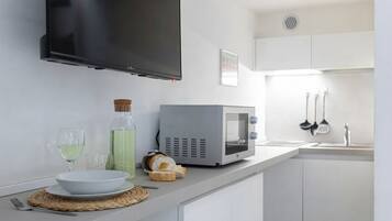 A kitchen with a flat-screen TV mounted above the counter, a microwave, and a sink with hanging utensils.