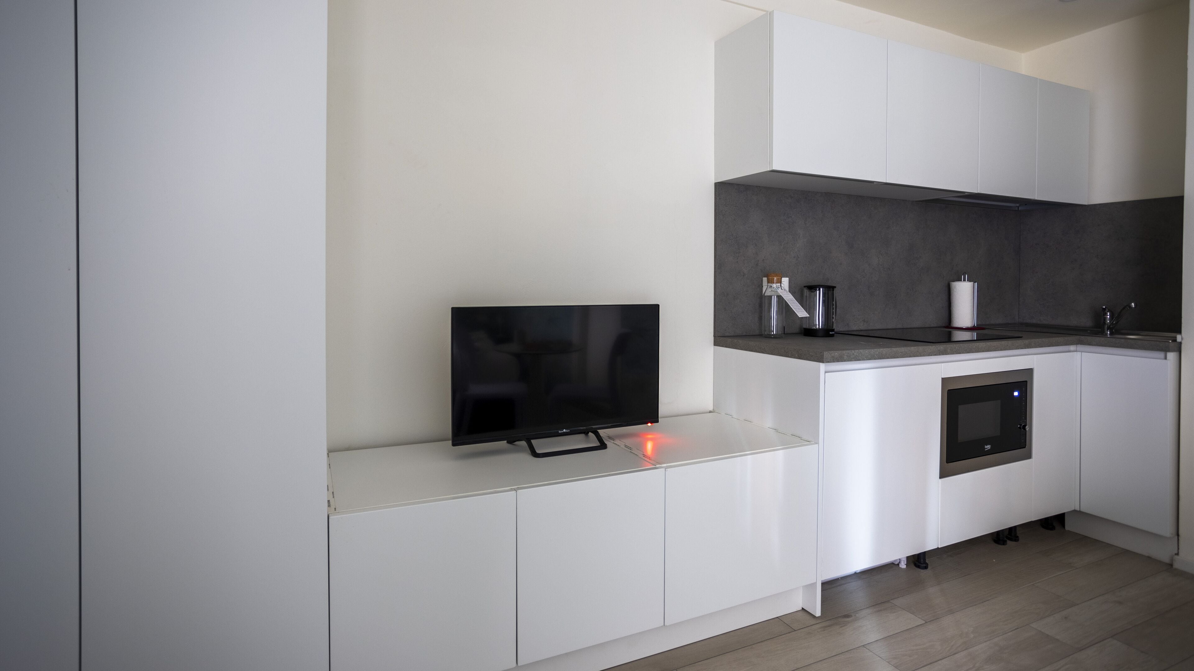 A modern kitchen with white cabinetry, a built-in oven, a microwave, and a flat-screen TV.