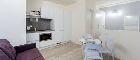 A compact living space with a kitchenette, a dining area with a table and chairs, and a purple sofa.
