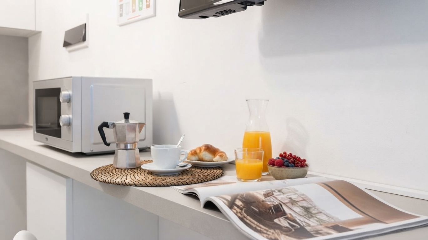 A breakfast setup with a coffee maker, a cup, a croissant, a glass of orange juice, and a bowl of berries on a counter.