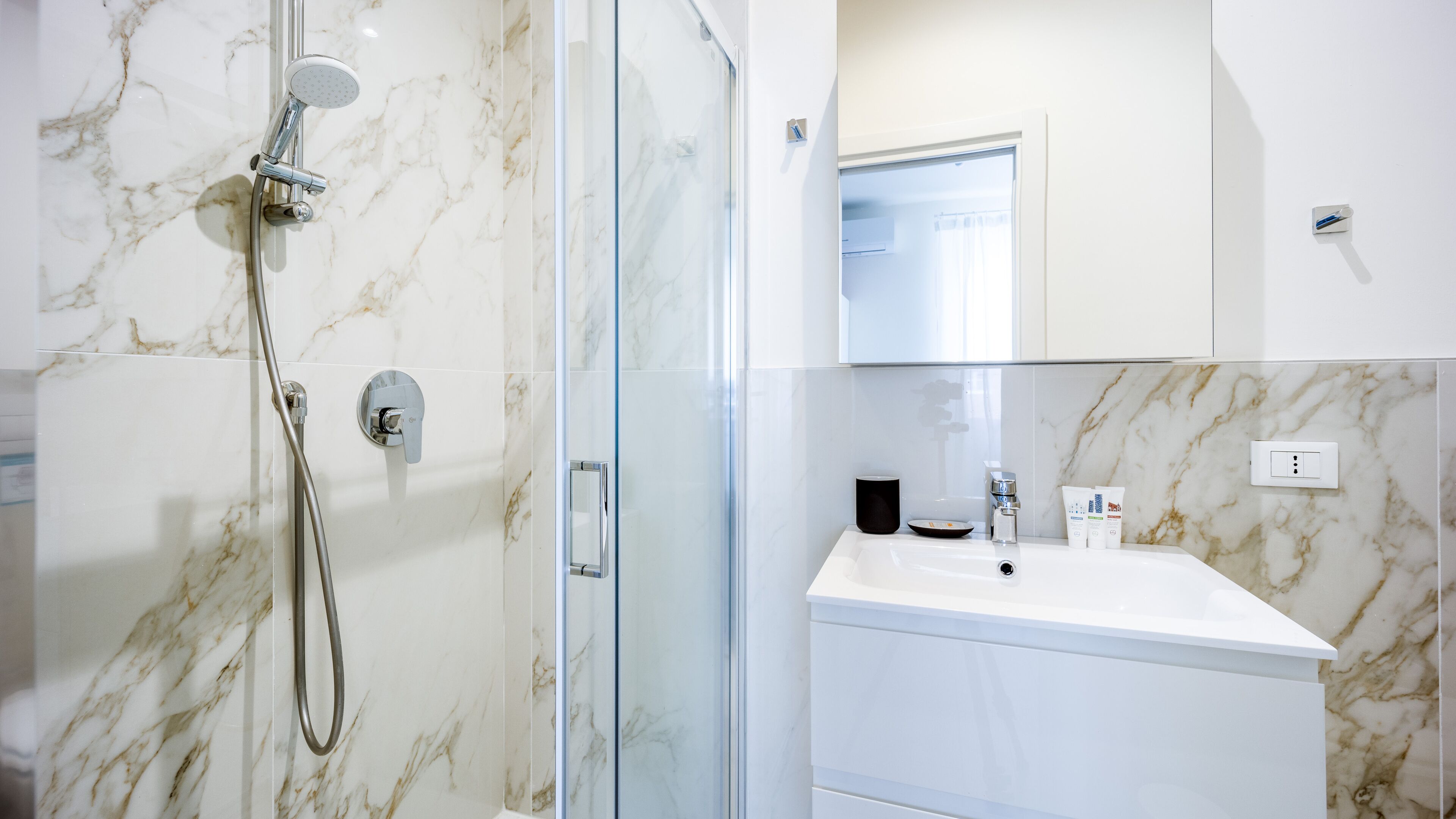 A modern bathroom with a glass-enclosed shower, a white sink, and a marble backsplash.