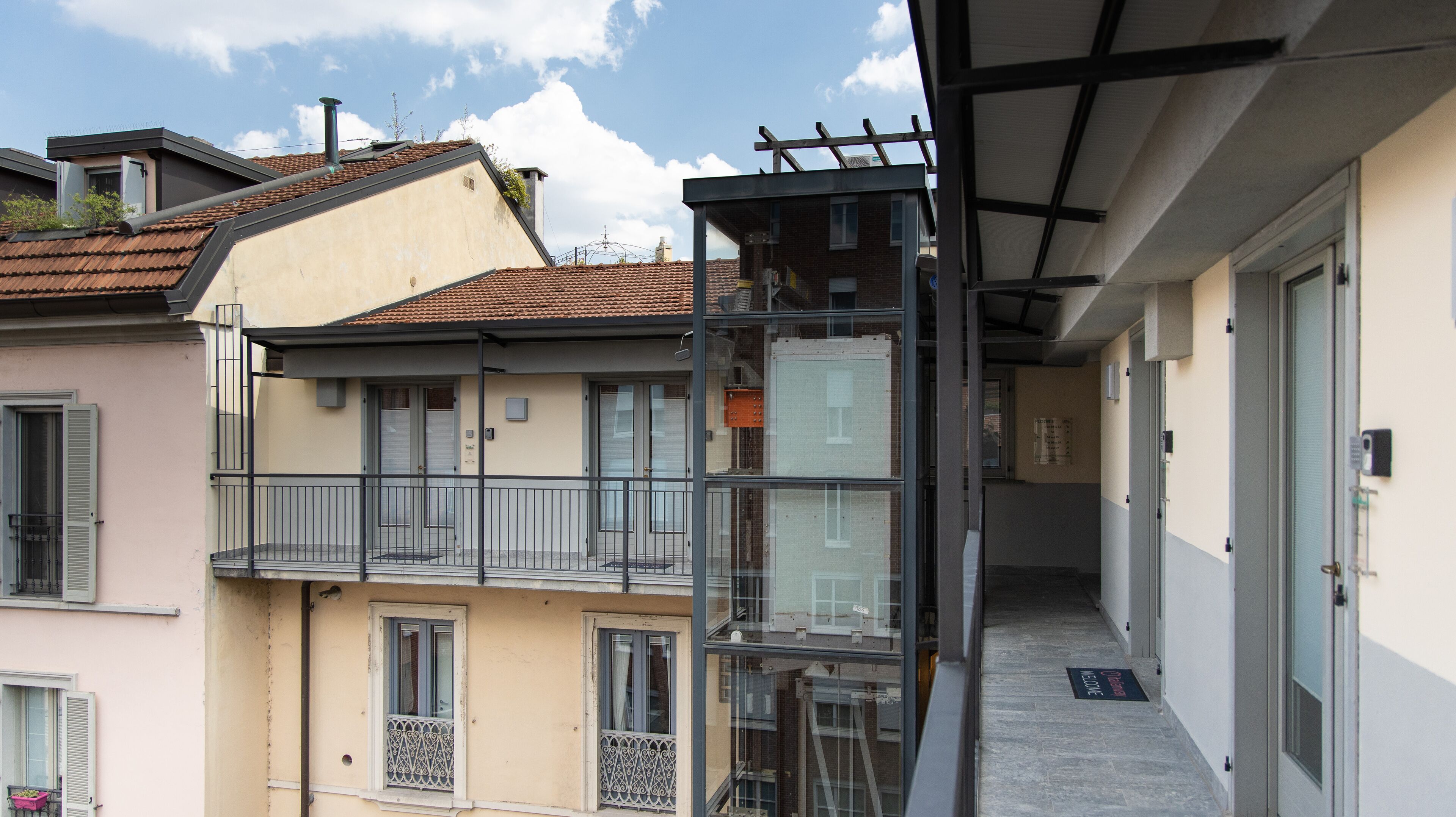 Un edificio de varios pisos con balcones, un corredor cubierto y una puerta con un felpudo que dice 'Bienvenido'.