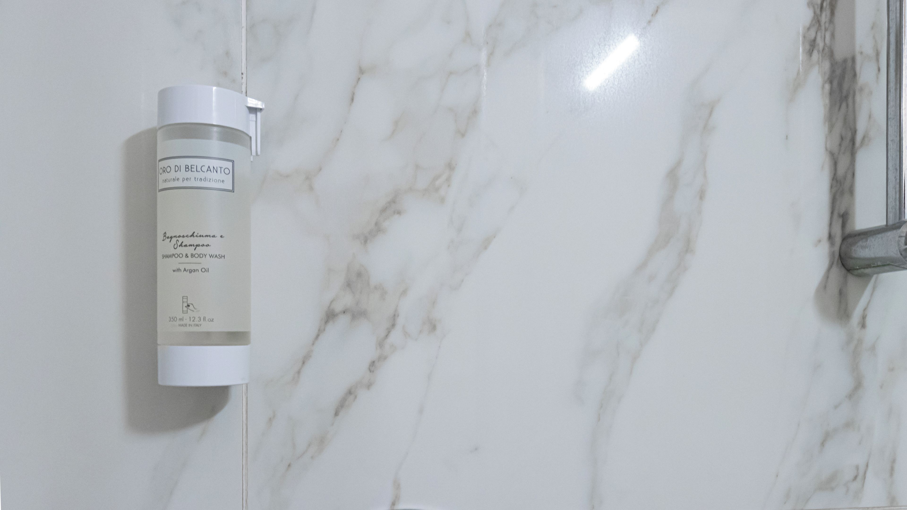 A bathroom with a marble wall and a bottle of shampoo on the wall.