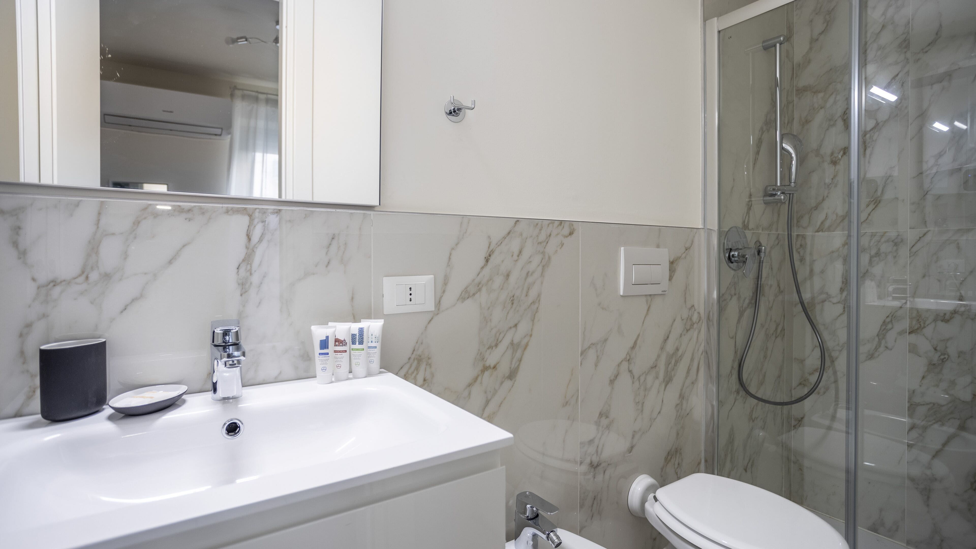 A bathroom with a white sink, a mirror, a shower, and marble walls.