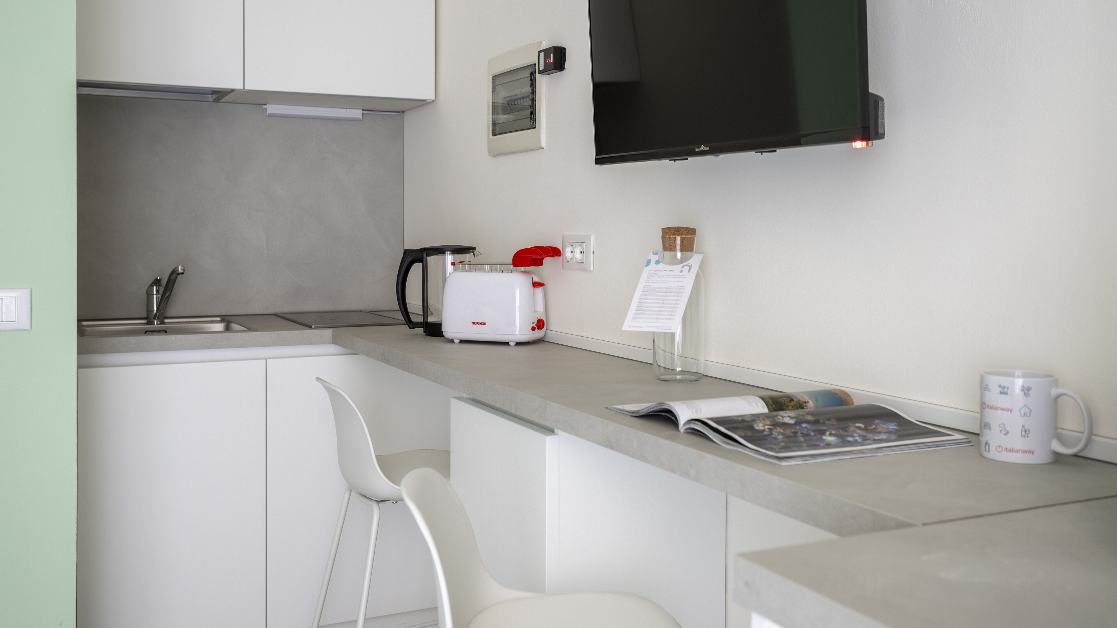 Una cocina moderna con armarios blancos, un tostador, una tetera y un televisor de pantalla plana montado sobre la encimera.