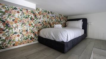 Une chambre à coucher avec un papier peint à motifs floraux, un lit recouvert de draps blancs et une tête de lit sombre.