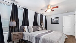 Un dormitorio con cama, mesita de noche, lámpara, ventilador de techo y una puerta.