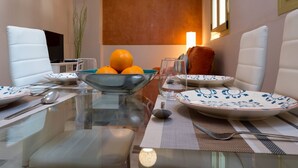 A dining table set with plates, bowls, and cutlery, with a bowl of oranges and glasses on it. - DescubreHome Macarena Town Center (Sevilla)