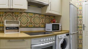 A compact kitchen with a microwave, oven, and washing machine. A sign advertises a bistro. - DescubreHome Macarena Town Center (Sevilla)