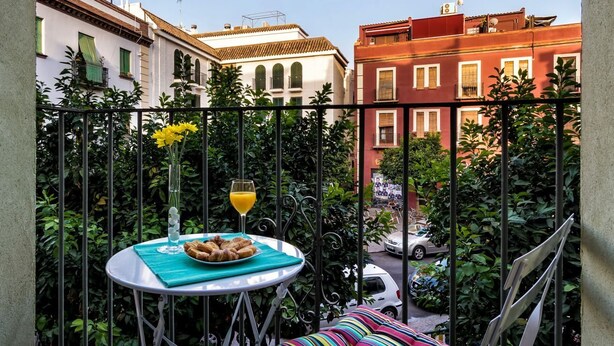 A balcony with a table set for breakfast, a chair, and a view of the street. - DescubreHome Macarena Town Center (Sevilla)