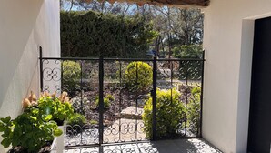 Ein überdachter Patio-Bereich mit einem Metallgitter, Topfpflanzen und einer Steinmauer im Hintergrund.