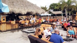Un área de bar al aire libre con mobiliario de mimbre y techo de paja.