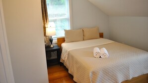 A bedroom with a bed, pillows, a nightstand, a lamp, and a window with blinds. - Stylish 4-bedroom whole house with plenty of parking (Catonsville)