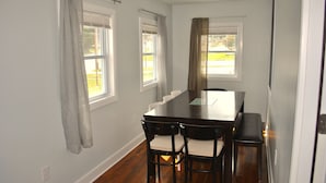 A dining area with a long table, four chairs, and two windows with curtains. - Stylish 4-bedroom whole house with plenty of parking (Catonsville)