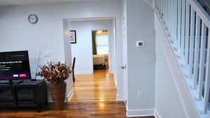 A living room with a flat-screen TV, a large potted plant, and hardwood flooring. - Stylish 4-bedroom whole house with plenty of parking (Catonsville)