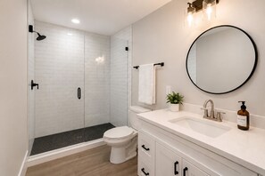 A modern bathroom with a shower, toilet, sink, and mirror.