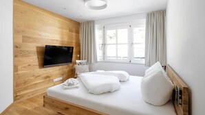 Une chambre moderne avec un mur en bois, un téléviseur à écran plat fixé au-dessus du lit, une fenêtre avec des rideaux et une table de chevet avec une lampe.