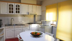 A compact kitchen with white cabinets, a microwave, a sink, and a dining table with chairs. - Charming and comfortable 380 m from the beach (Nazare)