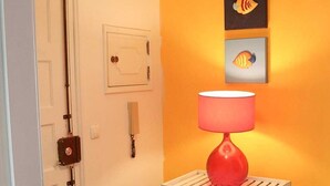 A hallway with a white door, a red lamp on a white table, and two framed artworks on the wall. - Charming and comfortable 380 m from the beach (Nazare)