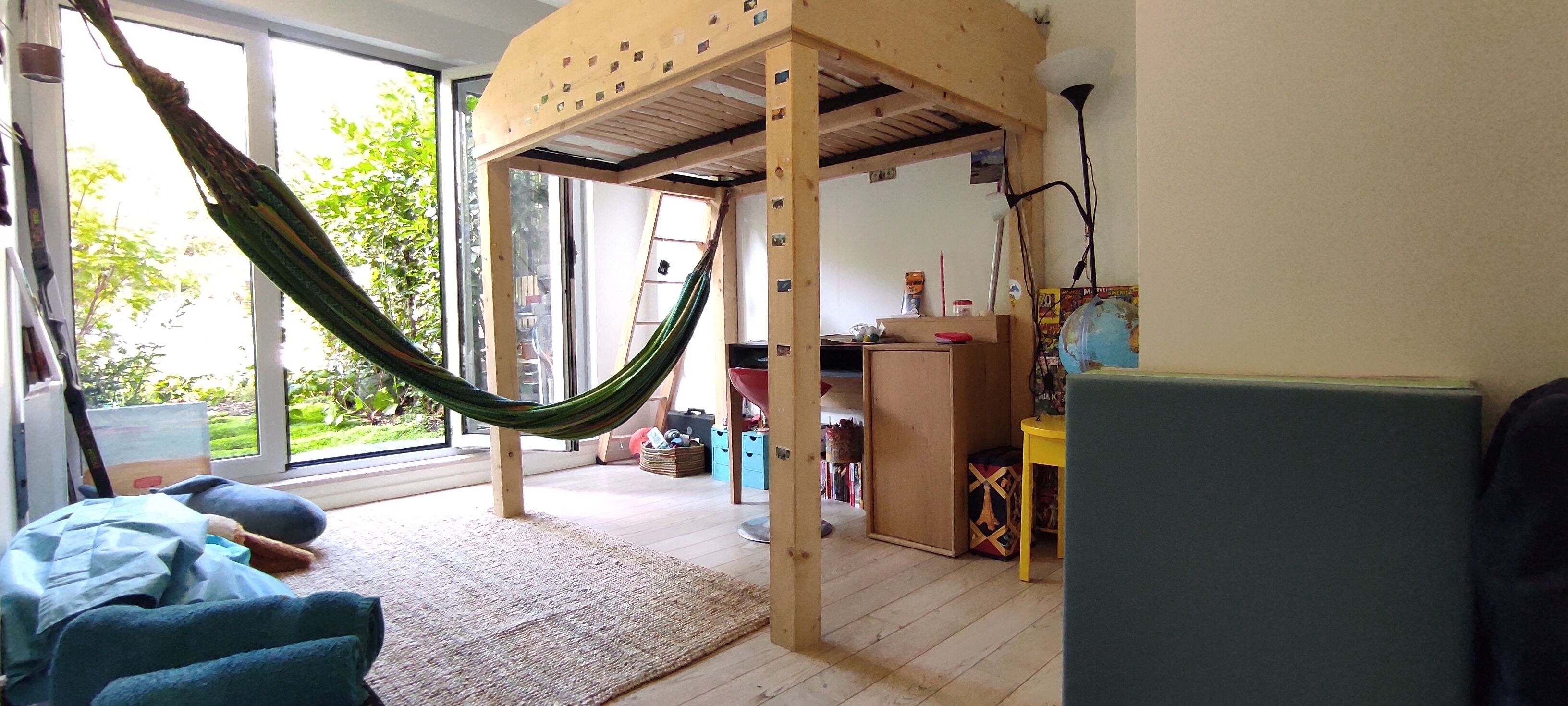 Une pièce avec un hamac, des meubles en bois, une petite table et une vue sur la verdure à l’extérieur.