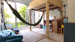 Ein Zimmer mit Hängematte, Holzmöbeln, einem kleinen Tisch und Blick auf Grünfläche.