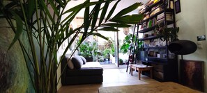 Ein gemütliches Wohnzimmer mit einem dunklen Sofa, einem Holztisch und einem Bücherregal voller Bücher und Pflanzen.