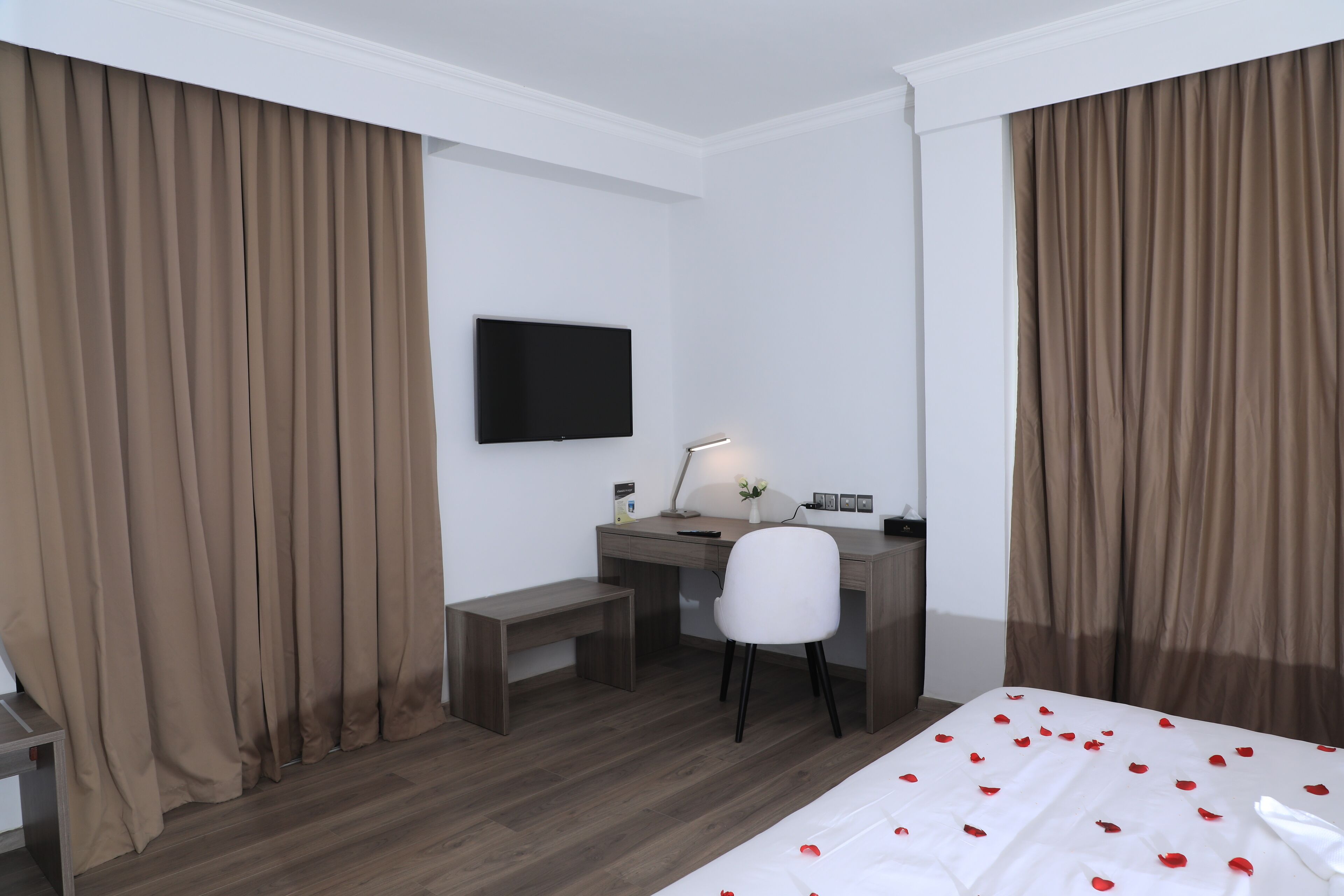 Una habitación de hotel con cama, escritorio, silla, televisor y cortinas.