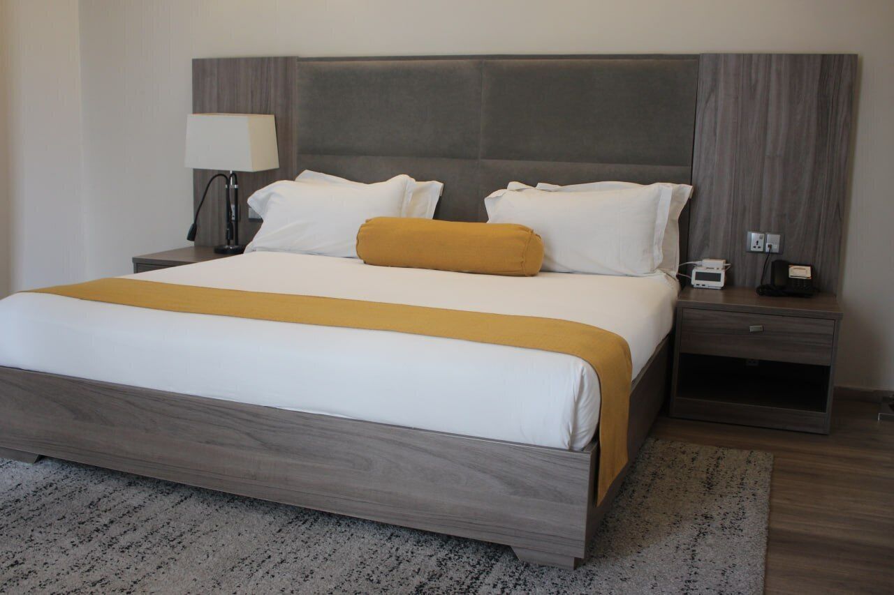 A modern hotel room with a large bed, a nightstand, a lamp, and a power outlet.